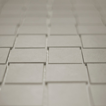 Les carreaux carrés sont disposés selon un motif de grille décalé, créant un subtil effet tridimensionnel. Les carreaux semblent