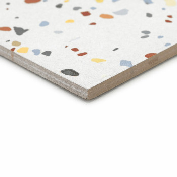 Een terrazzotegel ligt plat en vertoont kleurrijke, onregelmatige steenfragmenten op een lichtgrijs oppervlak, met een gladde, a