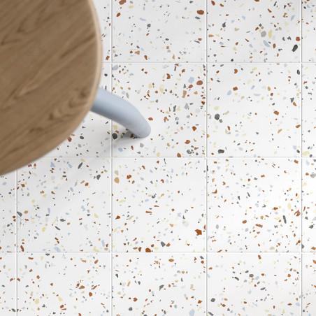 Vierkante tegels met een gespikkeld patroon van veelkleurige fragmenten liggen onder een houten tafel met een lichtblauwe poot, 