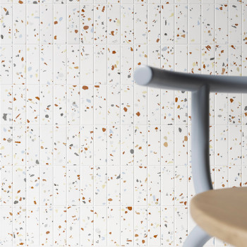 Los azulejos de terrazo muestran fragmentos de colores dispersos sobre un fondo blanco. En primer plano hay un asiento de madera