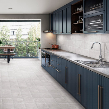 A modern kitchen features blue cabinets with sleek handles, a gray tiled backsplash, and a stone countertop. Sunlight filters th