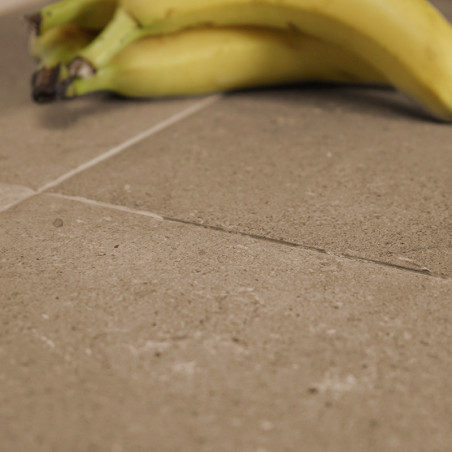 Les bananes reposent sur une surface de carrelage carrée lisse, brun clair, à la texture subtile. Le décor suggère un comptoir d
