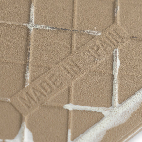 Un carreau de céramique marron texturé présente des lignes de grille en relief et le texte « MADE IN SPAIN », sur un fond uni.
