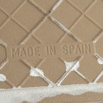 Beige ceramic tile features embossed text `MADE IN SPAIN,` displaying a diamond pattern with irregular white patches on the surf