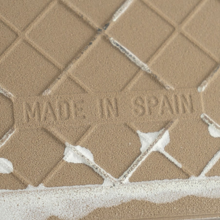 Beige ceramic tile features embossed text `MADE IN SPAIN,` displaying a diamond pattern with irregular white patches on the surf