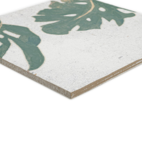 Um azulejo cerâmico exibe um motivo de folha verde sobre fundo branco. Sua borda é levemente chanfrada, destacando espessura e t