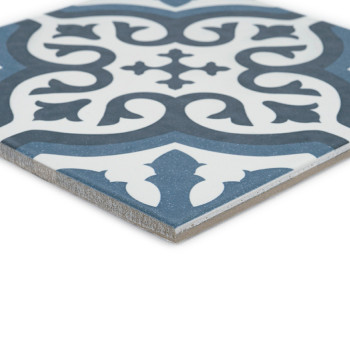 Le carreau présente un motif floral orné en bleu foncé et blanc, présentant des courbes symétriques et des feuilles stylisées su
