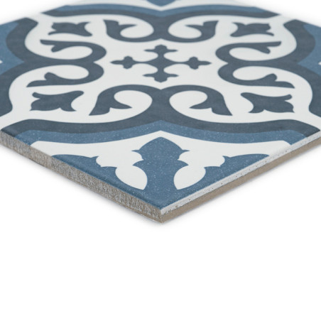 Le carreau présente un motif floral orné en bleu foncé et blanc, présentant des courbes symétriques et des feuilles stylisées su