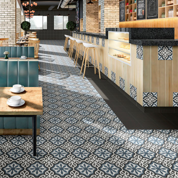 Verzierte blau-weiß gemusterte Fliesen bedecken den Boden eines Cafés und erstrecken sich bis zu einer Holztheke mit Barhockern 