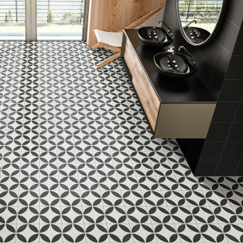 Black and white geometric tiles cover a bathroom floor with a circular pattern. black sinks and mirrors sit on a wooden vanity.