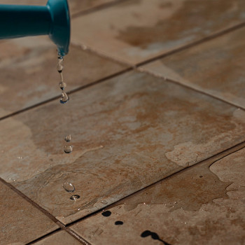 A água pinga de uma bica azul sobre azulejos marrons texturizados, criando pequenas poças e uma superfície molhada em um ambient