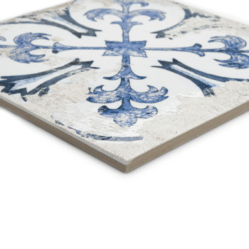 Un azulejo de cerámica presenta un patrón floral azul adornado sobre un fondo blanco, en ángulo para mostrar su superficie textu