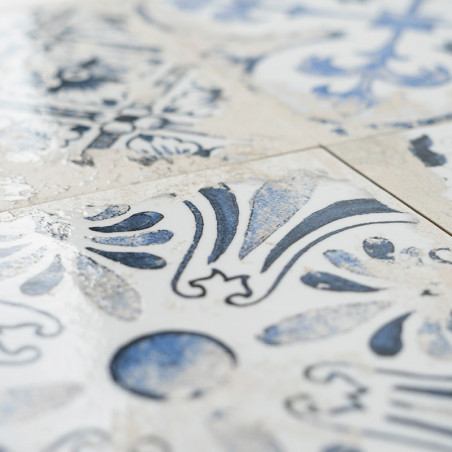 Un azulejo de cerámica muestra intrincados patrones florales y geométricos azules, dispuestos simétricamente, sobre un fondo bla