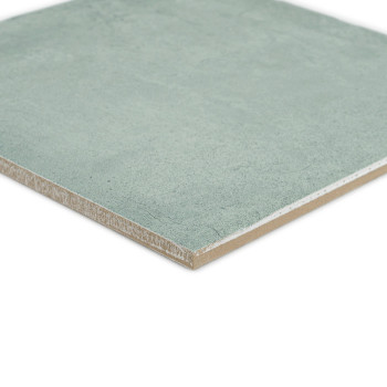Un azulejo cerámico cuadrada de color verde descansa sobre una superficie blanca, mostrando una textura suave y bordes ligeramen