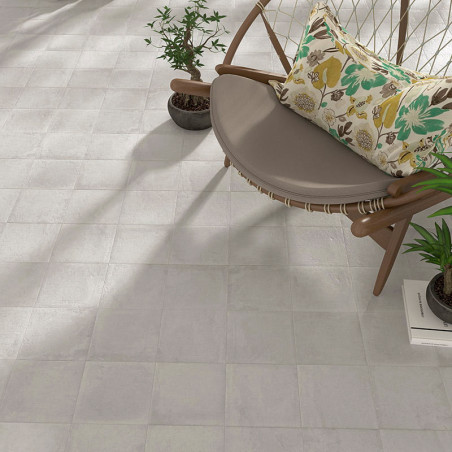 Un piso de mosaico beige se coloca horizontalmente, junto a una silla redonda y moderna con un cojín floral, rodeada de plantas 