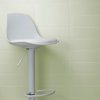 Vor einer hellgrün gefliesten Wand steht ein weißer, drehbarer Barhocker mit sichtbarem Hebel, der an ein klares, minimalistisch