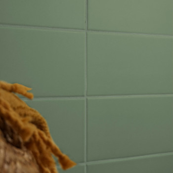 Een raster van groene rechthoekige tegels vormt een gladde wand, gedeeltelijk verborgen door de onscherpe textuur van bruine, ge