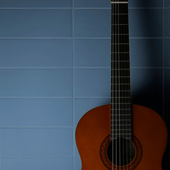 Um violão clássico fica de pé contra um fundo de azulejos quadrados azuis, lançando uma sombra suave na parede.