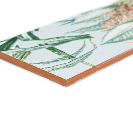 Um azulejo cerâmico exibe um padrão detalhado de folhas tropicais verdes e laranja, contra um fundo branco.