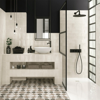 Un baño moderno cuenta con azulejos geométricas, una mampara de ducha de vidrio con marco negro, un lavabo sobre encimera blanco