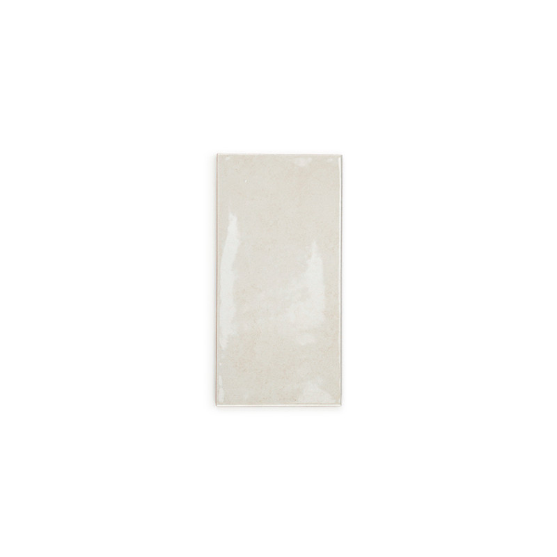 Un azulejo cerámico rectangular de color beige brillante se asienta sobre un fondo blanco liso y refleja la luz sutilmente en su