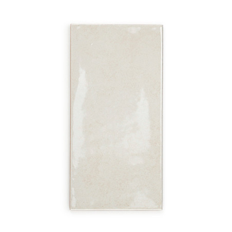 Un azulejo cerámico rectangular de color beige brillante se asienta sobre un fondo blanco liso y refleja la luz sutilmente en su