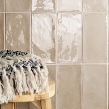 Los azulejos de color beige brillante reflejan la luz y crean una superficie brillante. Un taburete redondo de madera con un tej