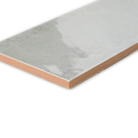 Un carreau de céramique rectangulaire présente une surface grise lisse et brillante avec un bord de couleur terre cuite, reposan