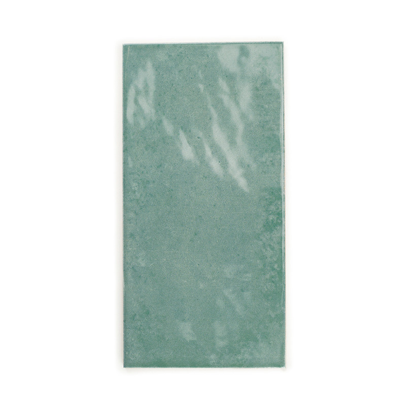 Le carreau de céramique rectangulaire avec une surface verte brillante reflète légèrement la lumière. Il repose sur un fond uni 