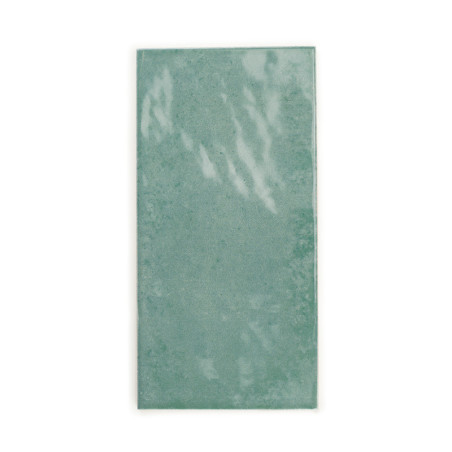 Azulejo cerámico rectangular con una superficie verde brillante que refleja ligeramente la luz. Se apoya sobre un fondo blanco l
