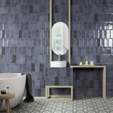 Azulejos rectangulares azules cubren la pared del baño, encima de un tocador con lavabo blanco y espejo ovalado, cerca de un pis