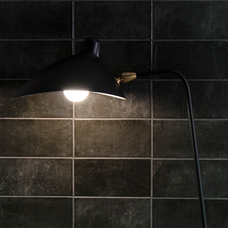 Eine schwarze Lampe beleuchtet dunkle, glänzend geflieste Wände. Das Licht erzeugt einen Kontrast zu den Fliesen und hebt ihre s