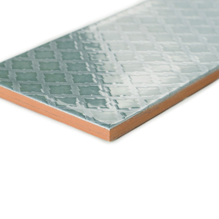 Un azulejo de cerámica muestra un patrón geométrico brillante con formas entrelazadas en tonos azul claro, sobre un fondo blanco
