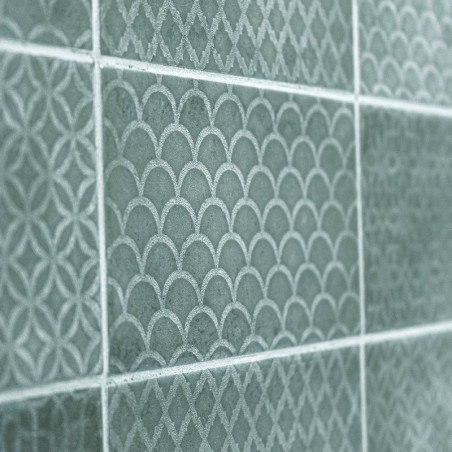 Les carreaux de céramique verte affichent des motifs complexes et répétitifs d’arcs et de losanges, créant une surface murale te