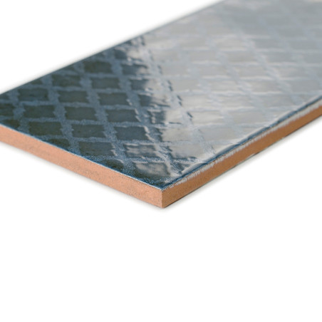 Um ladrilho cerâmico retangular apresenta uma superfície azul escura brilhante com um padrão geométrico sutil, colocado sobre um