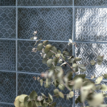 Keramische tegels vertonen ingewikkelde, gevarieerde geometrische patronen in een gedempte blauwachtige tint. Eucalyptustakken l