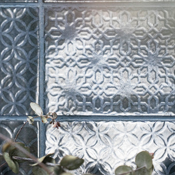 Dekorative Glasfliesen zeigen komplizierte geometrische Muster, die das Licht reflektieren. Im Vordergrund ruht ein Zweig kleine