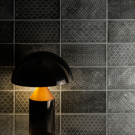 Una lámpara negra ilumina suavemente intrincados azulejos grises con patrones geométricos y festoneados en una habitación con po