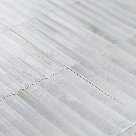 Les carreaux de céramique affichent une surface ondulée et texturée avec une couleur gris clair subtile. Ils sont disposés étroi