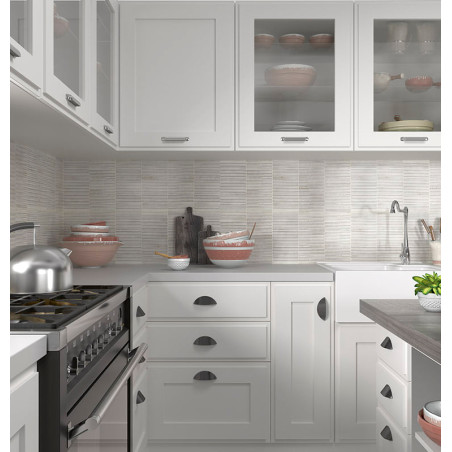 A cozinha possui armários brancos com portas de vidro contendo pratos. Bancada cinza lisa sob um backsplash de azulejos listrado