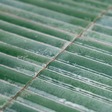 Groene tegels met een glanzende afwerking, gerangschikt in parallelle rijen, reflecteren licht. Hun oppervlaktetexturen creëren 