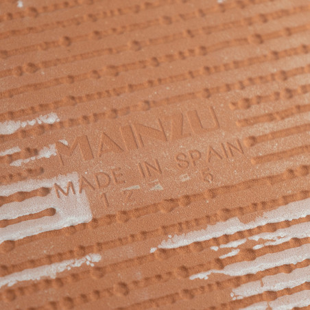 Een terracotta tegel, gestructureerd met verhoogde horizontale lijnen en witte vlekken, toont in het midden de tekst `MAINZU MAD