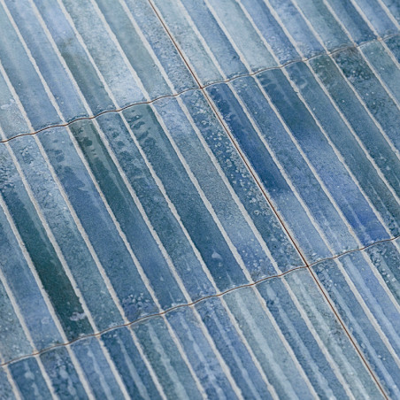 Blauwe rechthoekige tegels overlappen elkaar, waardoor een gestructureerd oppervlak ontstaat. Subtiele kleurvariaties en glans v