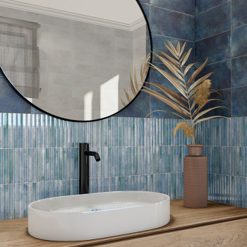 Op een houten aanrechtblad staat een witte ovale spoelbak met een zwarte kraan. Een grote ronde spiegel weerspiegelt blauwe tege