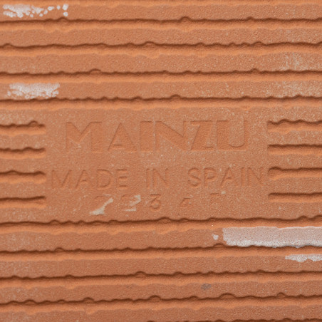Terracotta tegels tonen de tekst `MAINZU MADE IN SPAIN` in reliëf te midden van horizontale groeven, wat de oorsprong en product