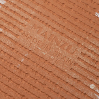 Op de terracotta tegel is in het midden de tekst `MAINZU MADE IN SPAIN` in reliëf weergegeven, omgeven door evenwijdige ribbels 