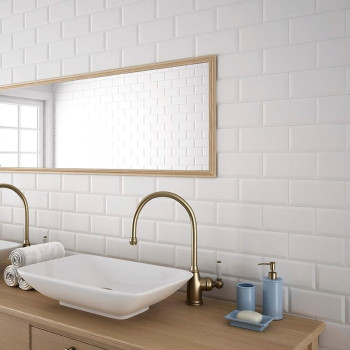 Los azulejos rectangulares blancos crean un telón de fondo limpio en un baño, que cuenta con un espejo con marco de madera, grif