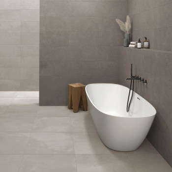 Een modern wit bad staat op grote beige tegels, grenzend aan een muur met een minimalistische inrichting, inclusief een houten k