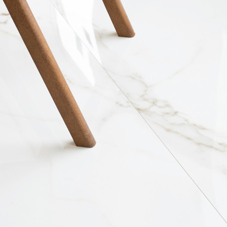 Un pied de table en bois repose sur un carrelage en marbre blanc brillant avec de subtiles veines grises, créant une atmosphère 