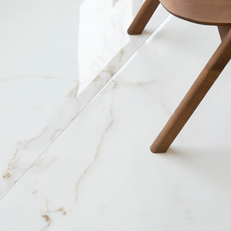Un carrelage blanc brillant avec de subtiles veines grises repose sur le sol, partiellement bordé par un pied de chaise en bois 